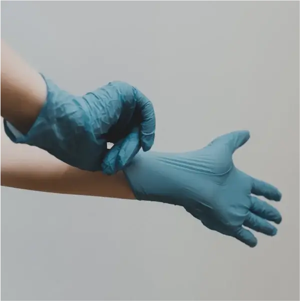 Крупный план человека, надевающего синие одноразовые перчатки на нейтральном фоне, передающий ощущение готовности и заботы о чистоте.
