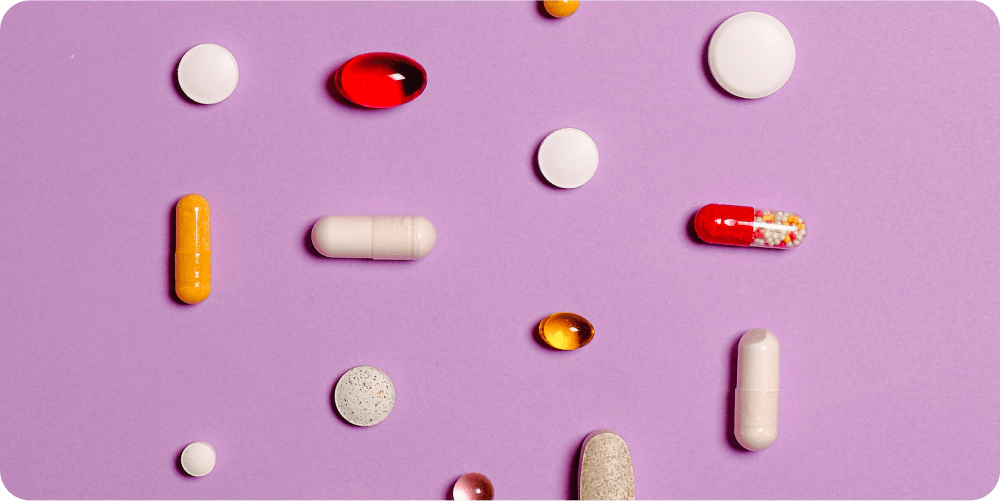 Разнообразные таблетки и капсулы разных форм, размеров и цветов разбросаны на фиолетовом фоне, передавая ощущение медицинского разнообразия и выбора.