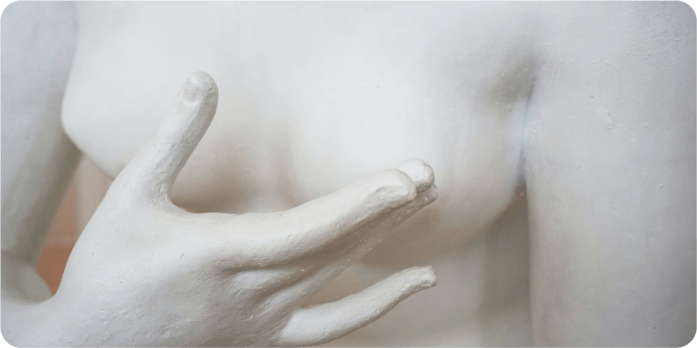 Крупный план статуи из белого мрамора с детальным жестом руки, расположенной у груди, передающей изящество и элегантность с помощью гладких, отполированных фактур.